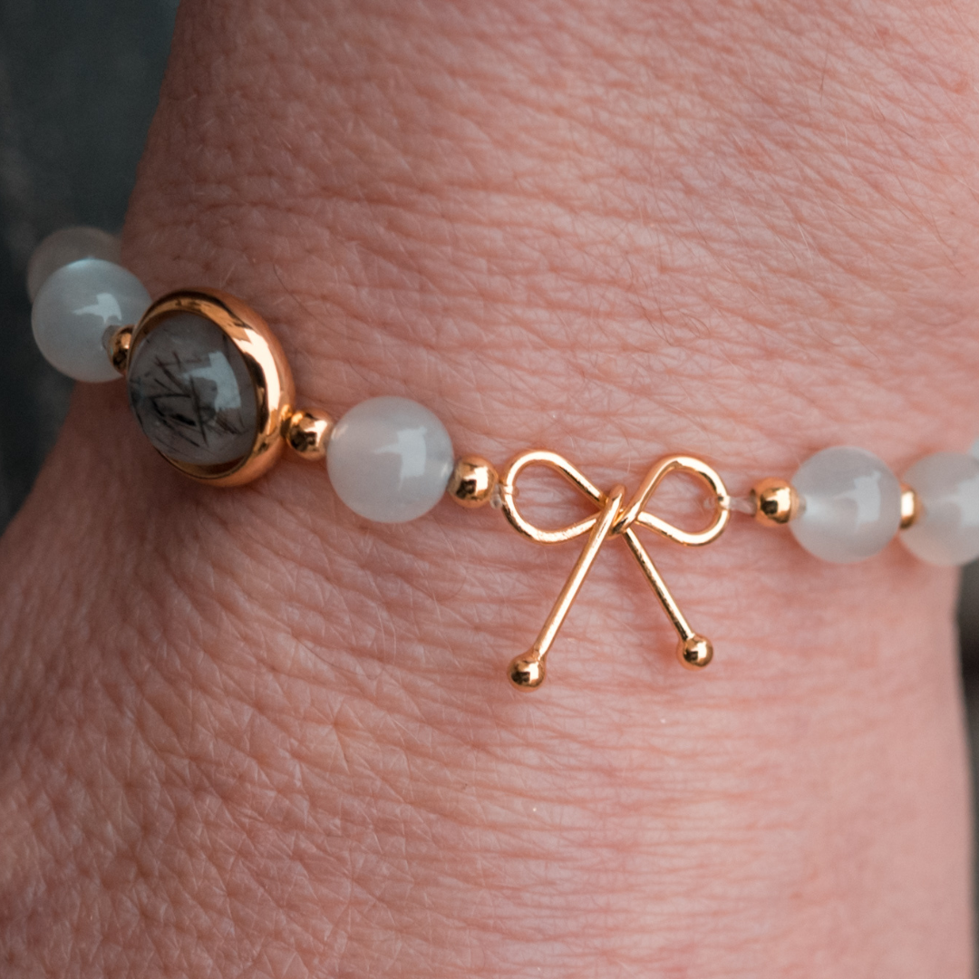 Bracelet anti-ménopause composé de pierre de lune, alternant avec de petites billes en or fin, avec une seule pierre de quartz rutile en son centre, entourée d'un anneau en or fin.